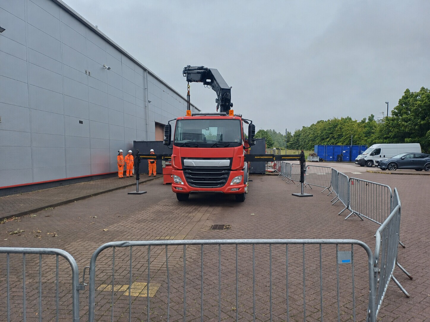 Lorry loader with stabilisers extended beside a warehouse and pedestrian barriers