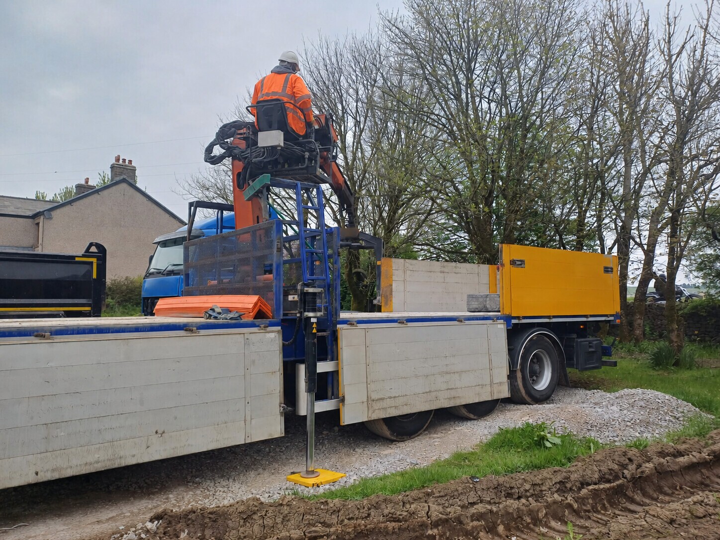Operator at the elevated controls of a lorry loader on a blue flatbed truck