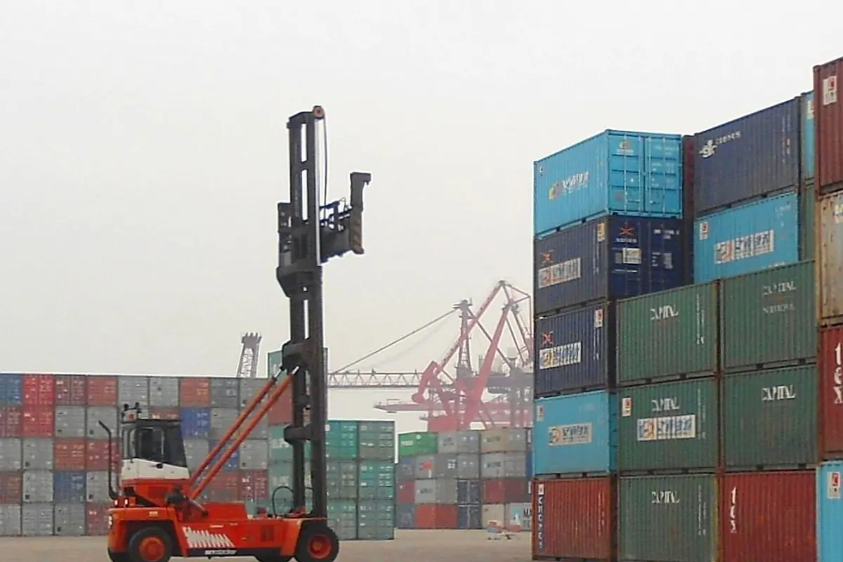 Empty-container handler with a vertical mast beside stacked containers